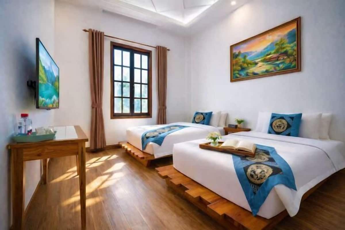 Una habitación de hotel con dos camas, televisión, ventana con cortinas y un cuadro en la pared.