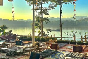 Un espace extérieur paisible, aménagé avec des coussins et des tables, offrant une vue sur un lac et des montagnes.