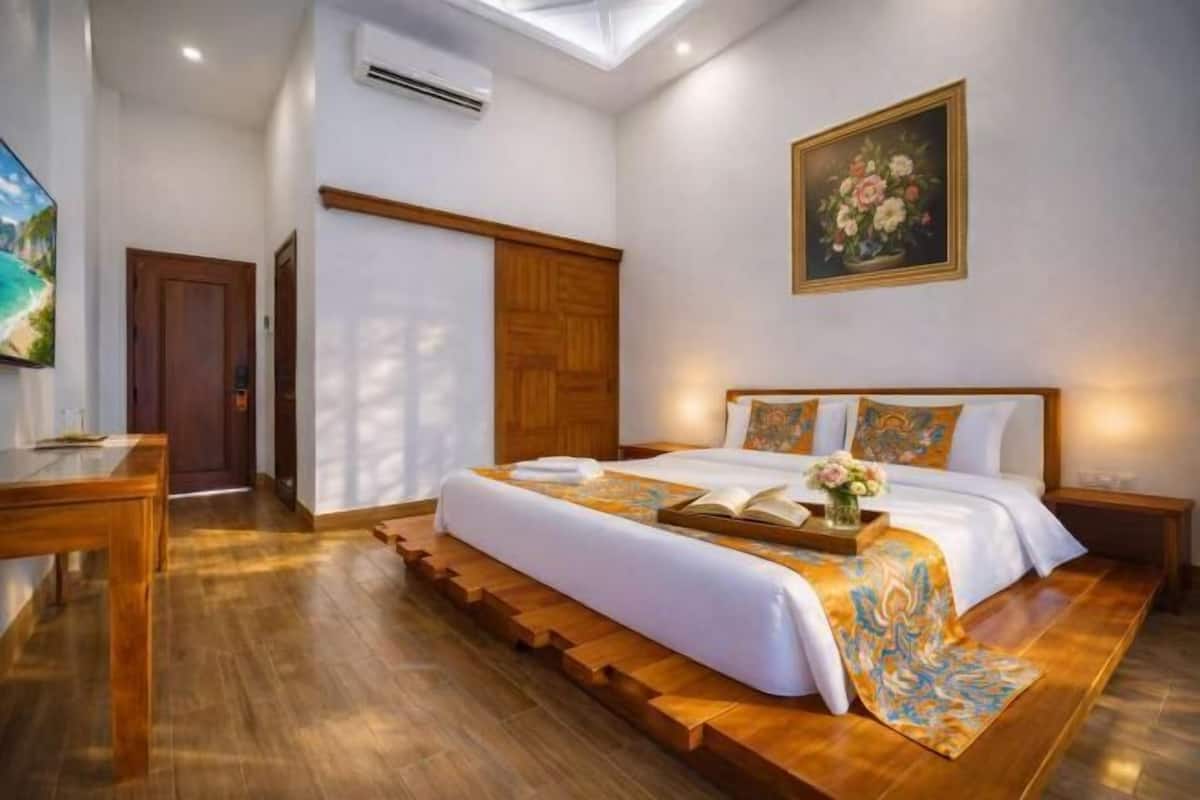 Un dormitorio con una cama grande, suelo de madera, un cuadro en la pared y un escritorio con una silla.