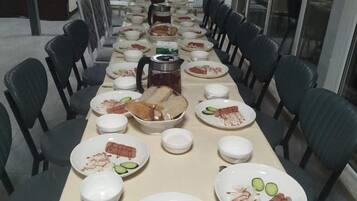 A long dining table set with plates, bowls, and a coffee pot, surrounded by chairs.
