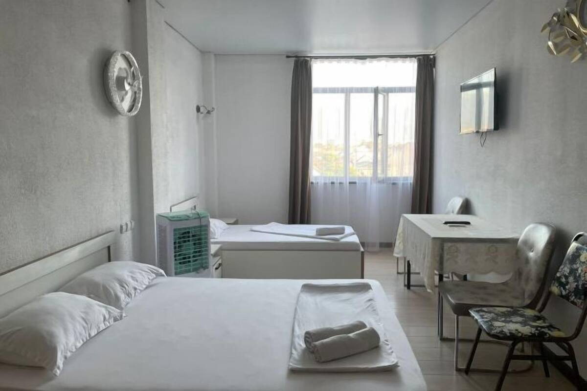 Ein Hotelzimmer mit Bett, Schreibtisch, Stuhl, Fernseher und einem Fenster mit Vorhängen.