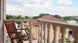 A balcony with a wooden chair, a balustrade, and a view of houses and trees. - Central Asia Inn Hotel (Almaty)