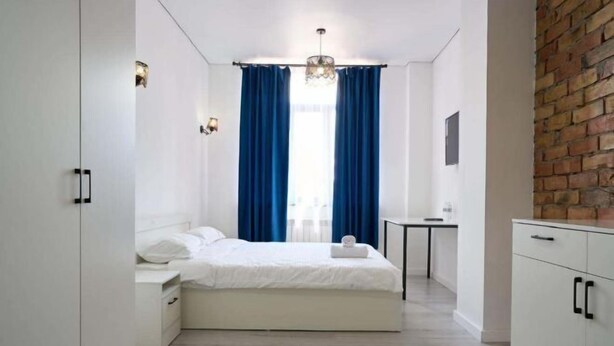 A bedroom with a bed, bedside table, and a small desk. - Central Asia Inn Hotel (Almaty)