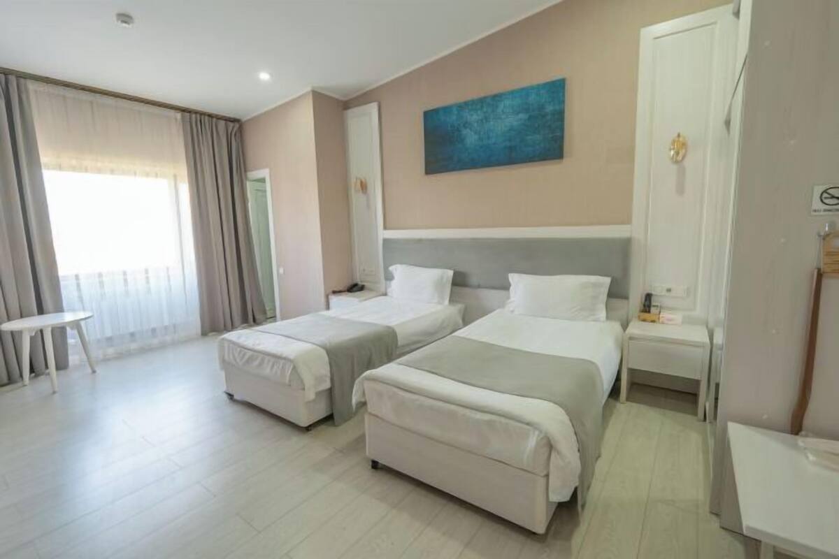 Ein Hotelzimmer mit zwei Betten, einem kleinen Tisch, einem Bild an der Wand und Blick ins Freie.