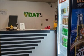 A reception desk with a sign that reads '7DAY' and a refrigerator stocked with beverages. - Central Asia Inn Hotel (Almaty)