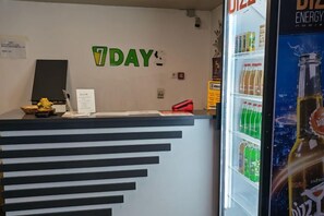 Uma receção com um letreiro que diz '7DAY' e um frigorífico cheio de bebidas.