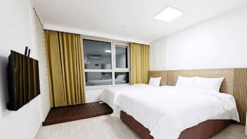 A hotel room with a bed, a TV, a window with curtains, and a wooden headboard.