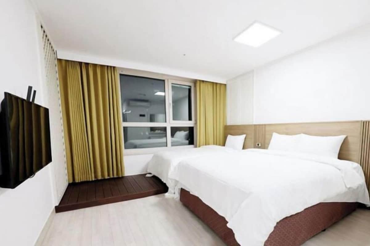 A hotel room with two beds, a television, a window with curtains, and a wooden headboard.