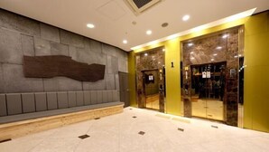 Een moderne lobby met een stenen muur, een houten bank en een glazen lift.