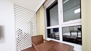 Een kamer met een houten tafel en stoelen, een raam met uitzicht op een bed, en een wit lattenroomscheiding.
