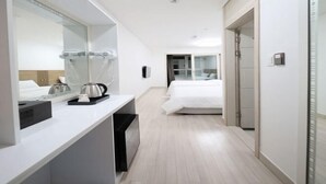 Een hotelkamer met een bed, nachtkastje, spiegel, koffiezetapparaat en een prullenbak.