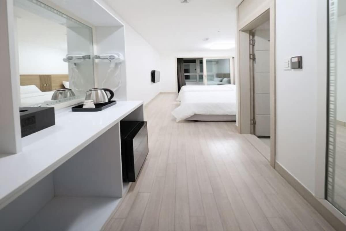A hotel room with a bed, a bedside table, a mirror, a coffee maker, and a trash bin.
