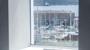 A marina with boats docked, a building in the background, and a window with a view of the marina. - Harbour View - 2 Bedroom Apartment - Milford Haven (Milford Haven)