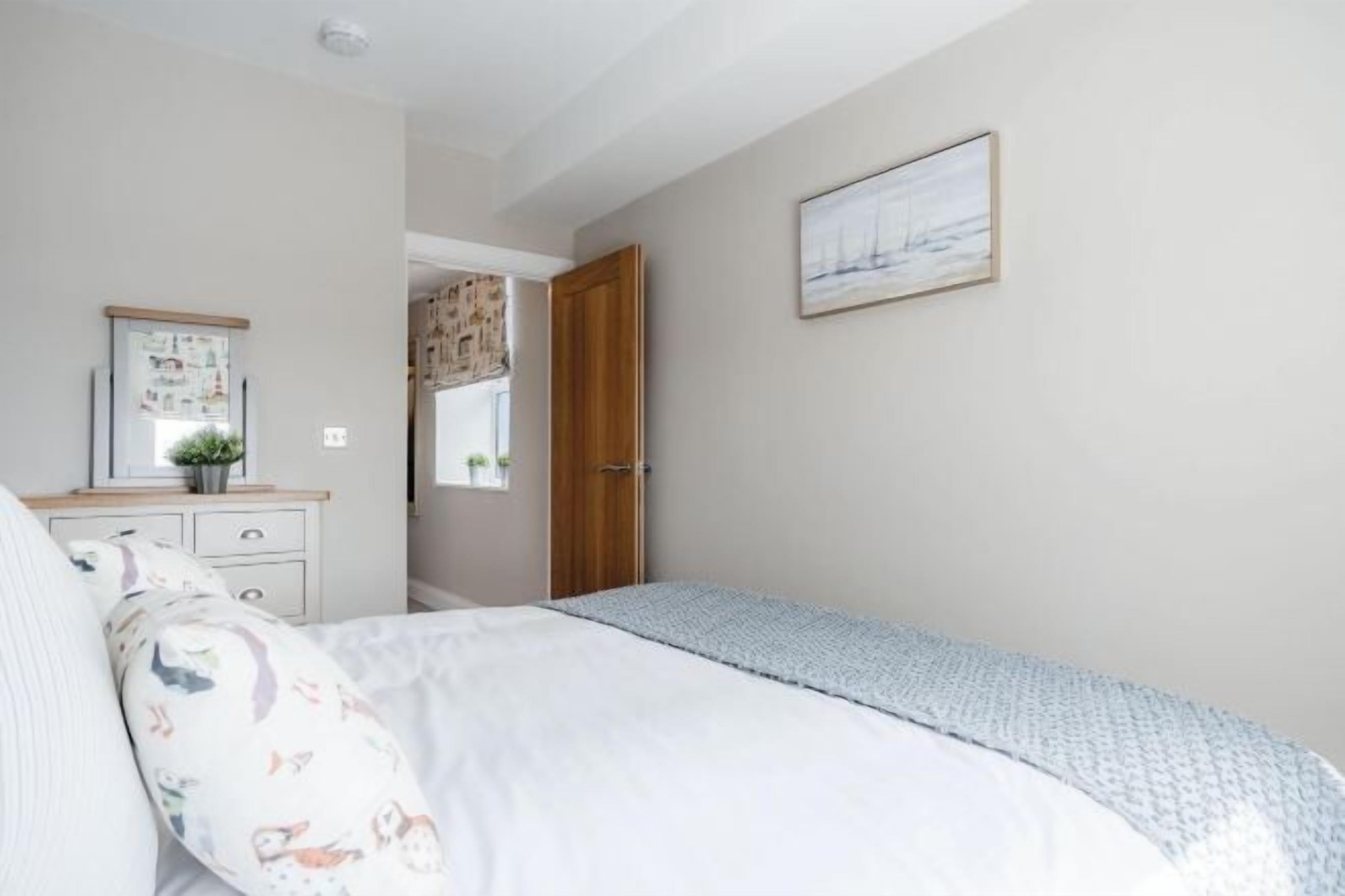 A bedroom with a bed, a dresser, a door, and a wall-mounted picture.