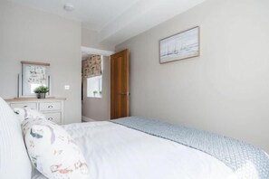 A bedroom with a bed, a dresser, a door, and a wall-mounted picture. - Harbour View - 2 Bedroom Apartment - Milford Haven (Milford Haven)