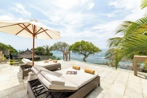 A sunlit outdoor lounge area with a large umbrella, lounge chairs, and a view of the ocean. - Nagasutra Villa by Nakula (Bali)