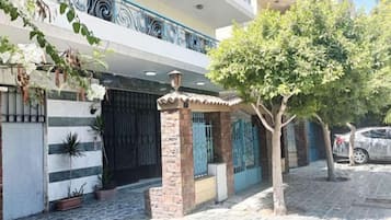 Un edificio residencial con entrada protegida por una reja, plantas en macetas y un árbol en primer plano.
