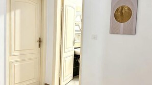 Un couloir avec une porte fermée, une porte ouverte donnant sur une salle de bain et une œuvre d’art encadrée accrochée au mur.