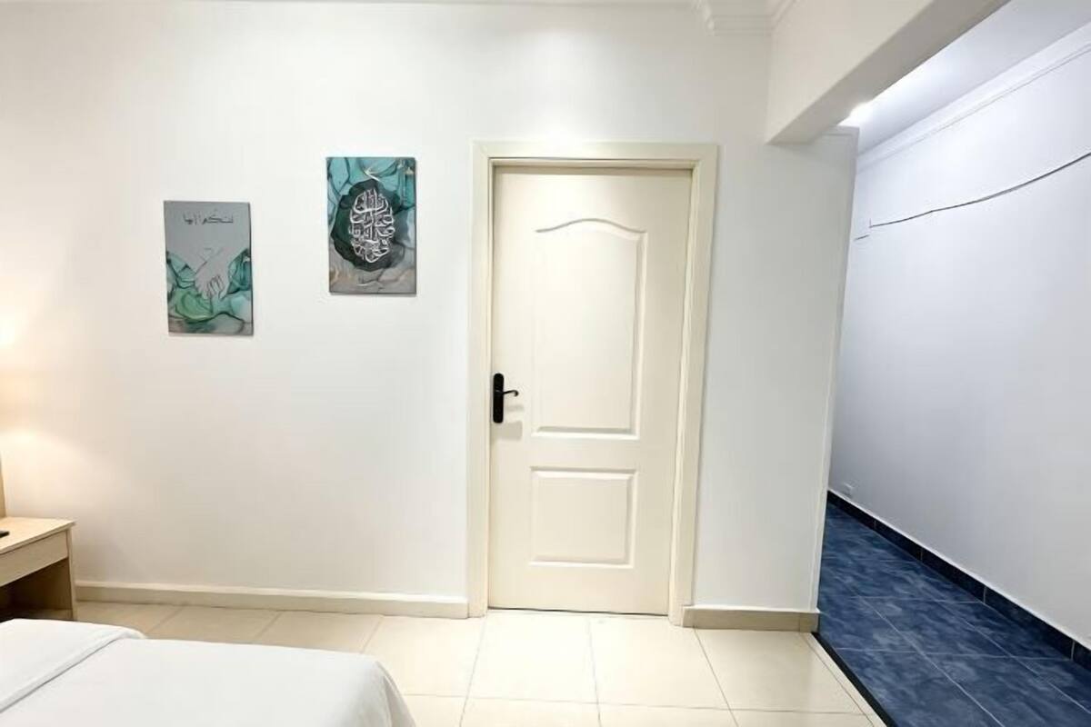 A hotel room with a bed, a door, and two wall-mounted artworks.