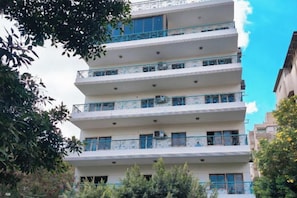 Un edificio de varios pisos con balcones, unidades de aire acondicionado y un cielo despejado.