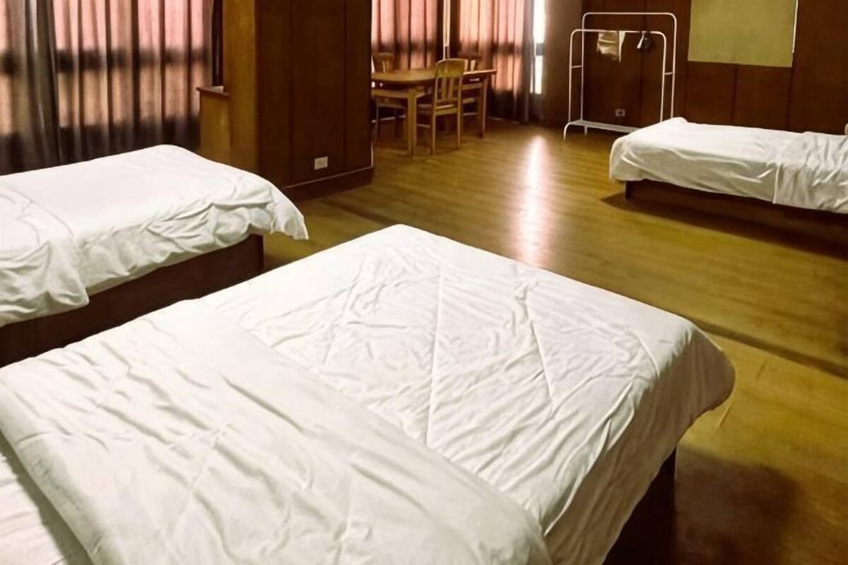 A hotel room with three beds, a wooden floor, a table with chairs, and a wardrobe.