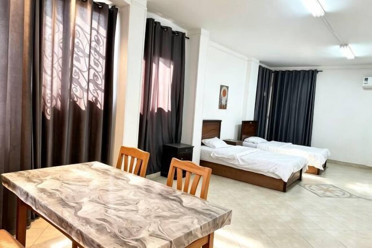 A hotel room with a dining table, two beds, and a small desk.