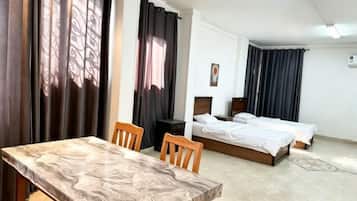 A hotel room with a dining table, two beds, and a small desk.