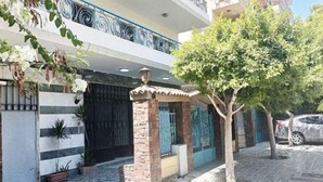 Un immeuble résidentiel doté d’une entrée sécurisée par un portail, de plantes en pot et d’un arbre au premier plan.