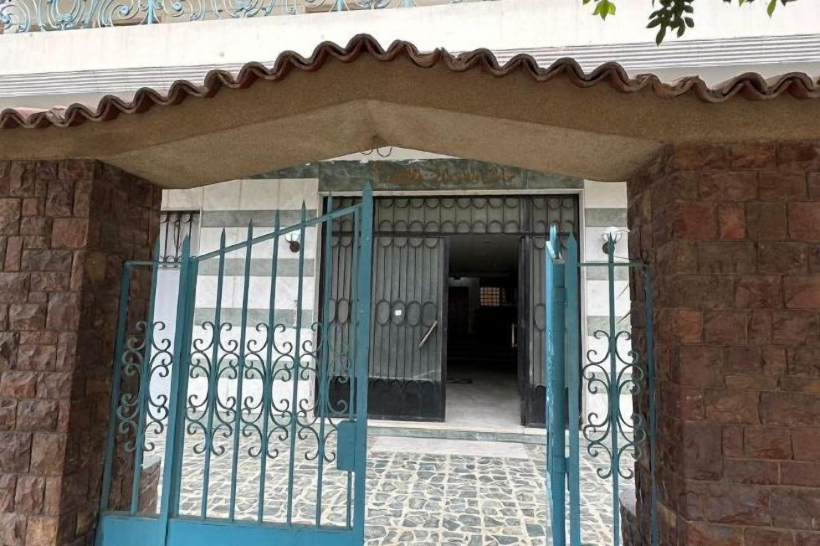 A gated entrance with a metal gate and a tiled floor leading to a building.