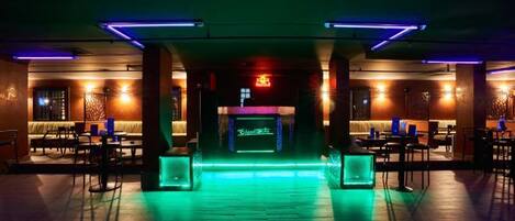 A bar area with a neon sign, wooden flooring, and ambient lighting.
