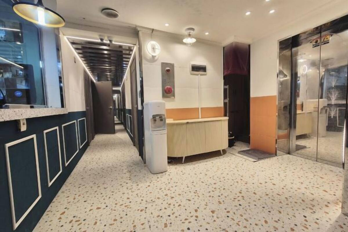 A hotel corridor with a reception desk, a clock, a radiator, and a glass elevator.