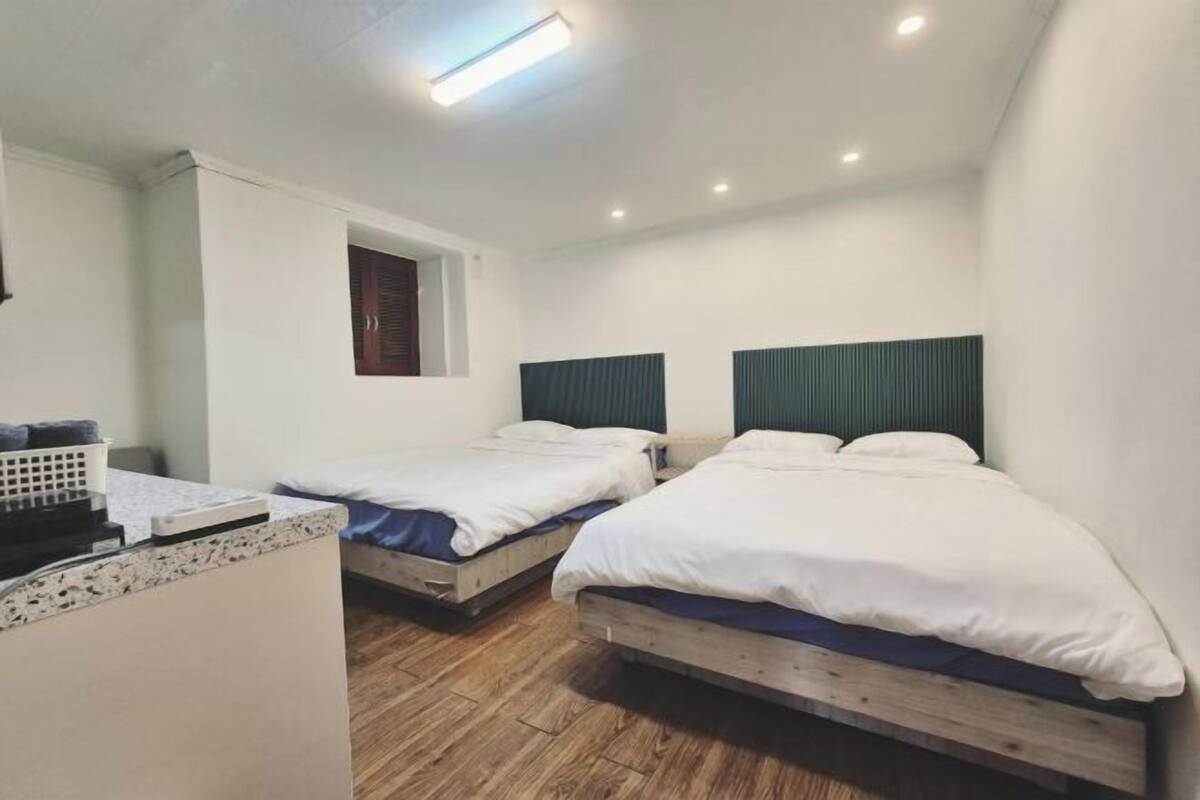 A room with two single beds, a small desk, and a window with blinds.