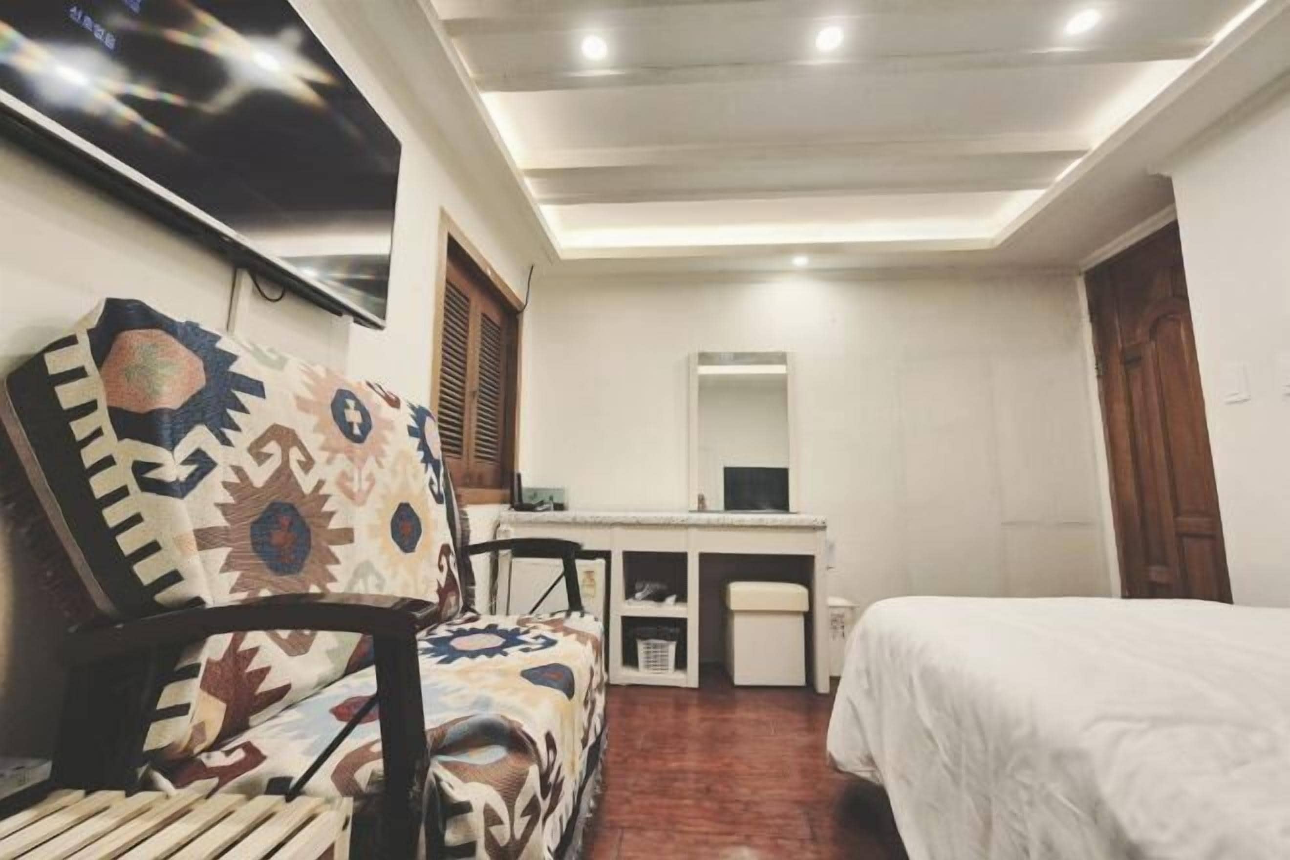 Um quarto com uma cama, uma escrivaninha, uma cadeira, uma televisão e um espelho.