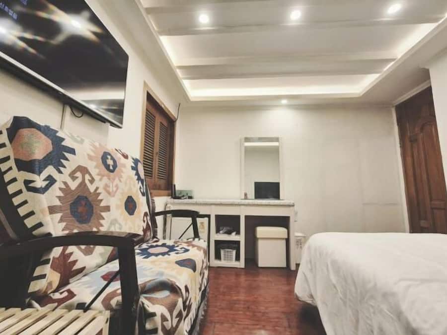 Um quarto com uma cama, uma escrivaninha, uma cadeira, uma televisão e um espelho.