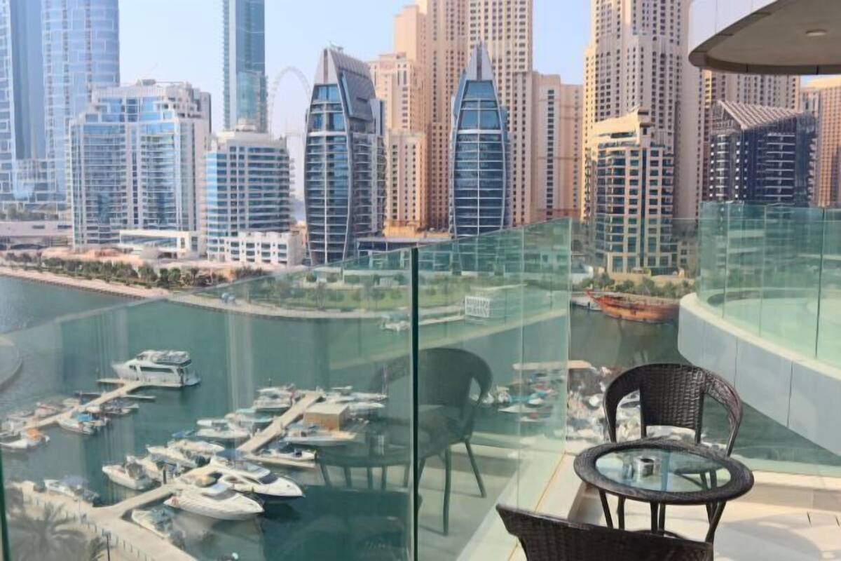 A high-rise building with a glass balcony overlooking a marina with boats.