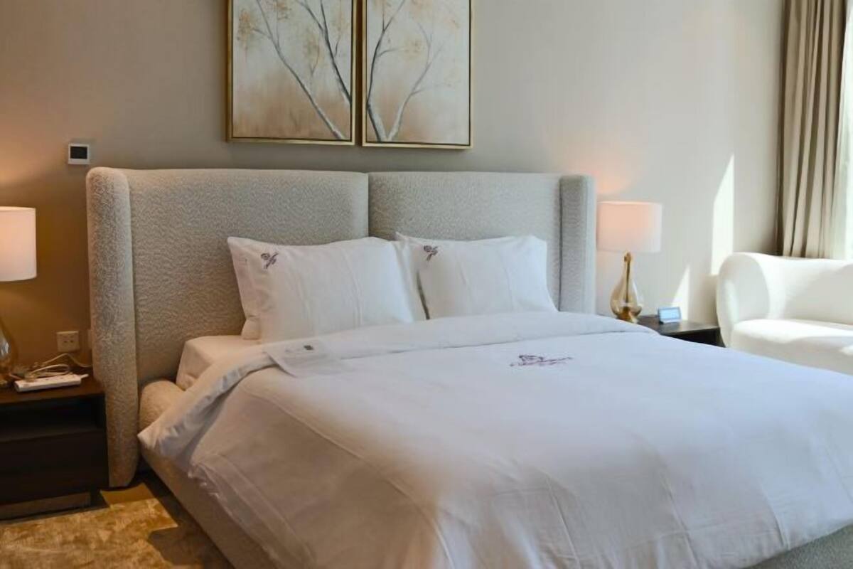 A hotel room with a large bed, two bedside tables, a chair, and artwork on the wall.