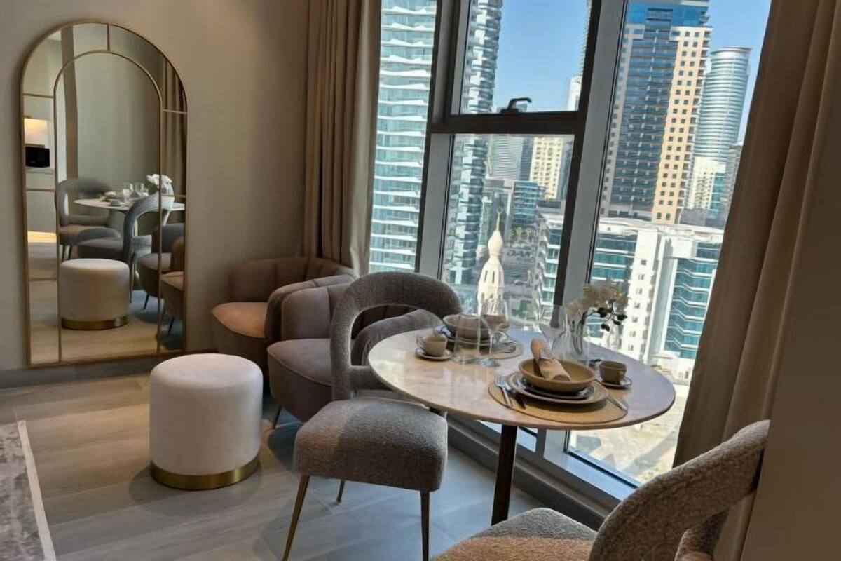 A modern hotel room with a dining area, a round table, and a view of the cityscape.