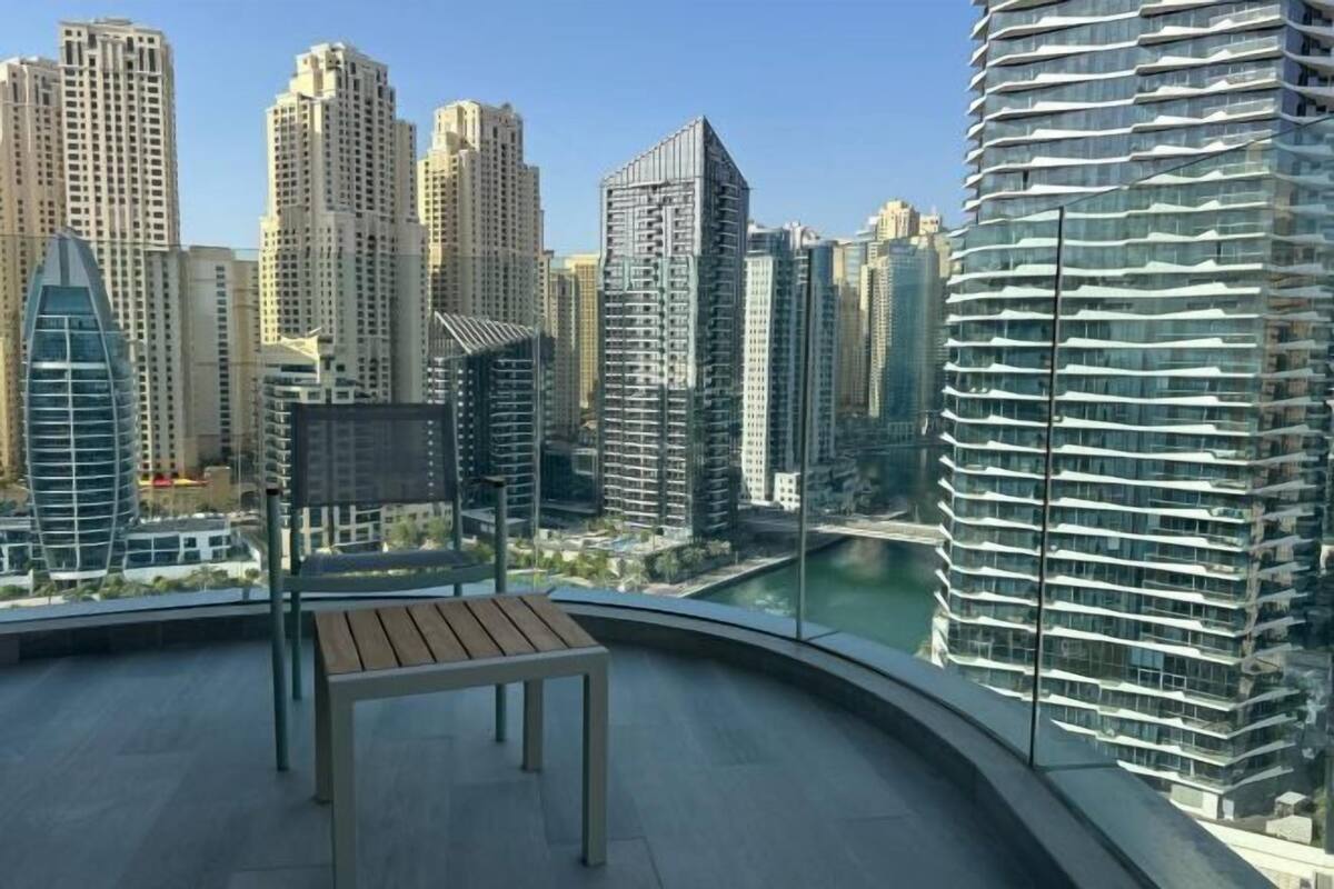 A high-rise building with a curved balcony, a wooden bench, and a view of other tall buildings and a river.