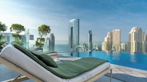 Una habitación de hotel moderna con piscina privada, vista al horizonte de la ciudad y un área de estar con un sillón verde acolchado.