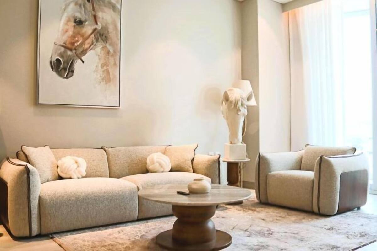 A living room with a beige sofa, a round coffee table, and a painting of a horse on the wall.
