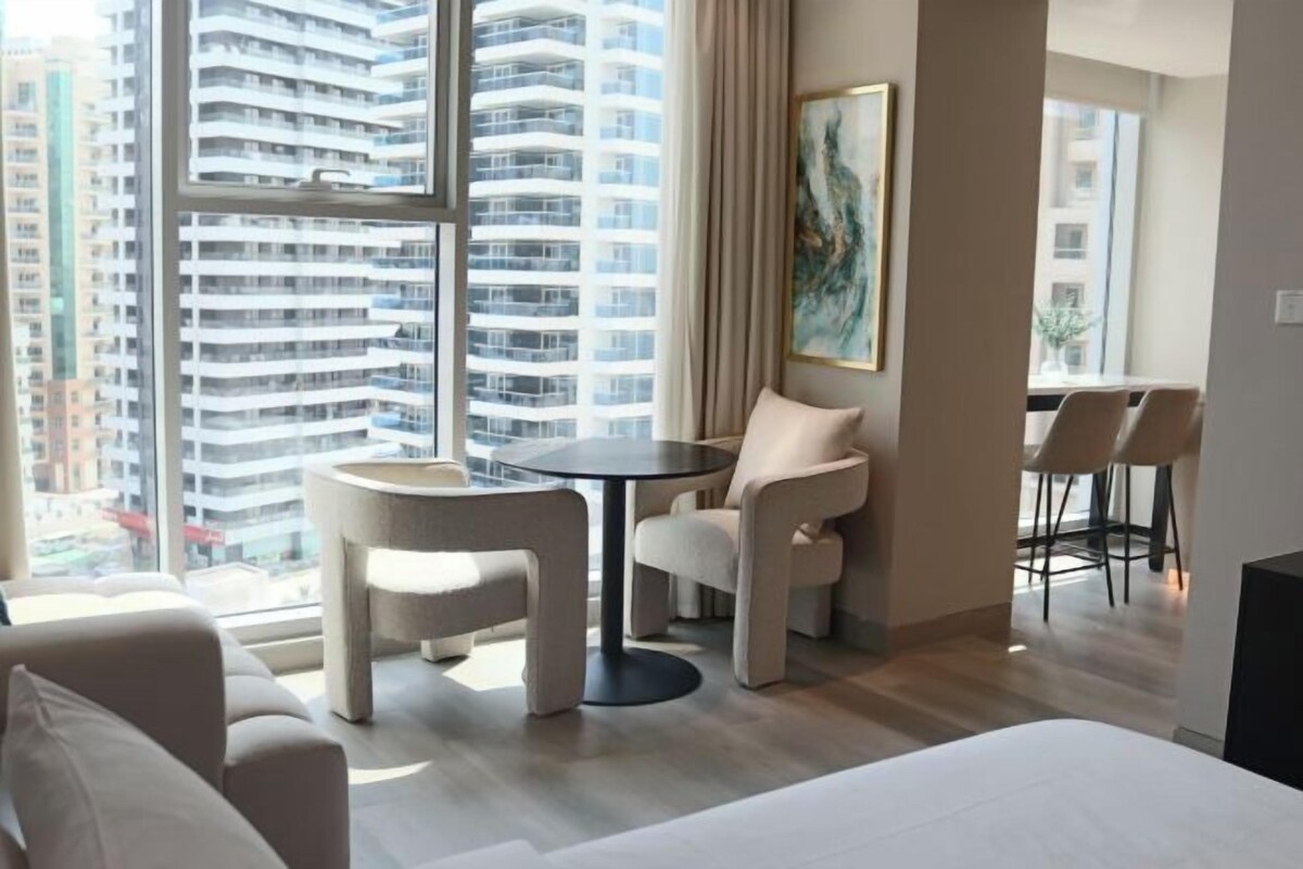 A modern hotel room with a large window, a round table, a sofa, and a bed.