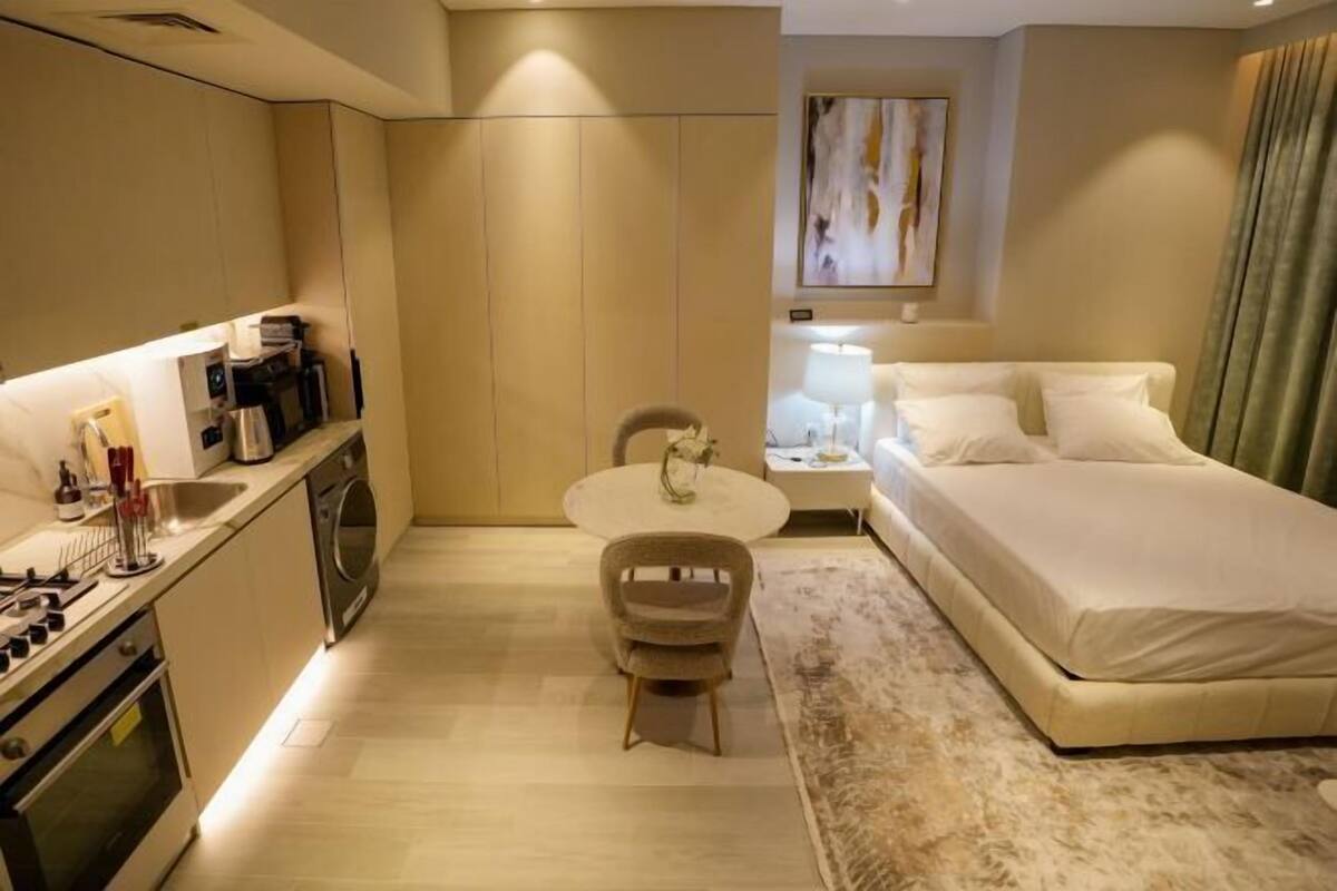 A compact hotel room with a kitchenette, a bed, a small round table, and a chair.