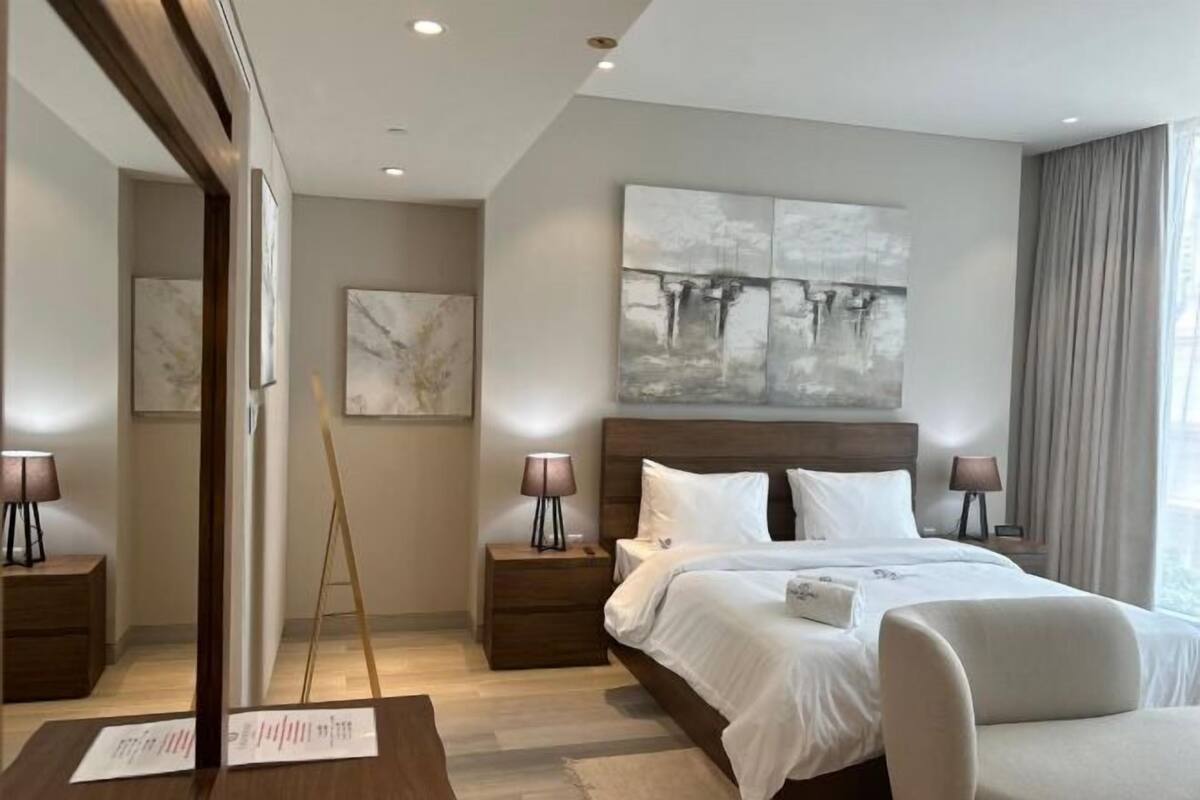 A modern hotel room with a large bed, two bedside tables with lamps, a wooden headboard, and abstract wall art.