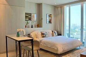 Habitación de hotel moderna con cama, escritorio y silla. En la pared hay cuadros enmarcados y vistas a la ciudad a través de amplias ventanas.