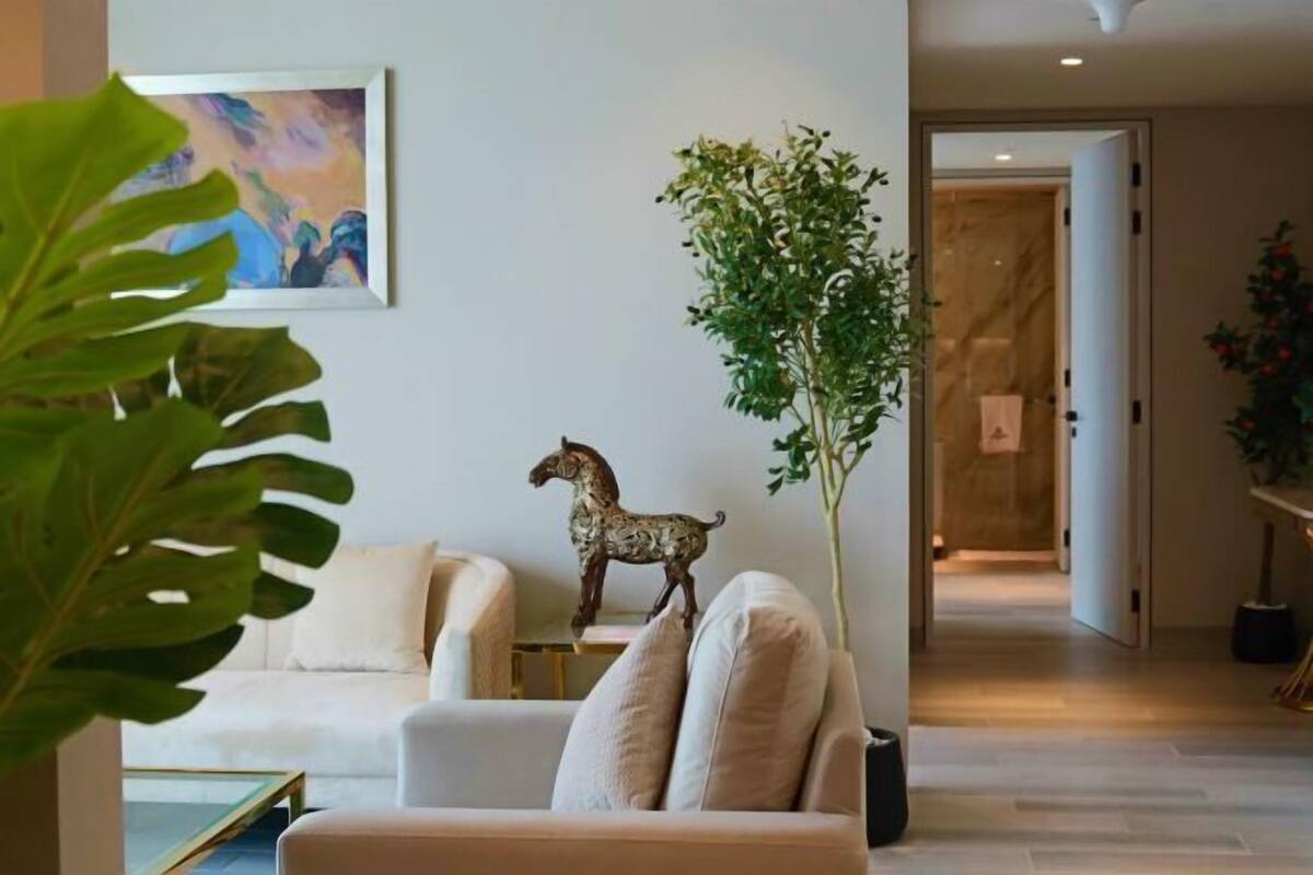 A modern living room with a sofa, a decorative horse statue, a large plant, and a painting on the wall.