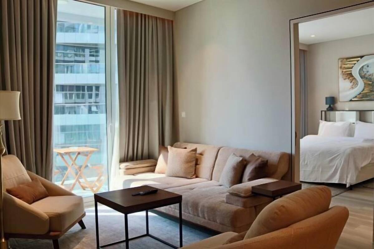 A hotel room with a sofa, armchair, a small table, a bed, and a view of a building through the window.