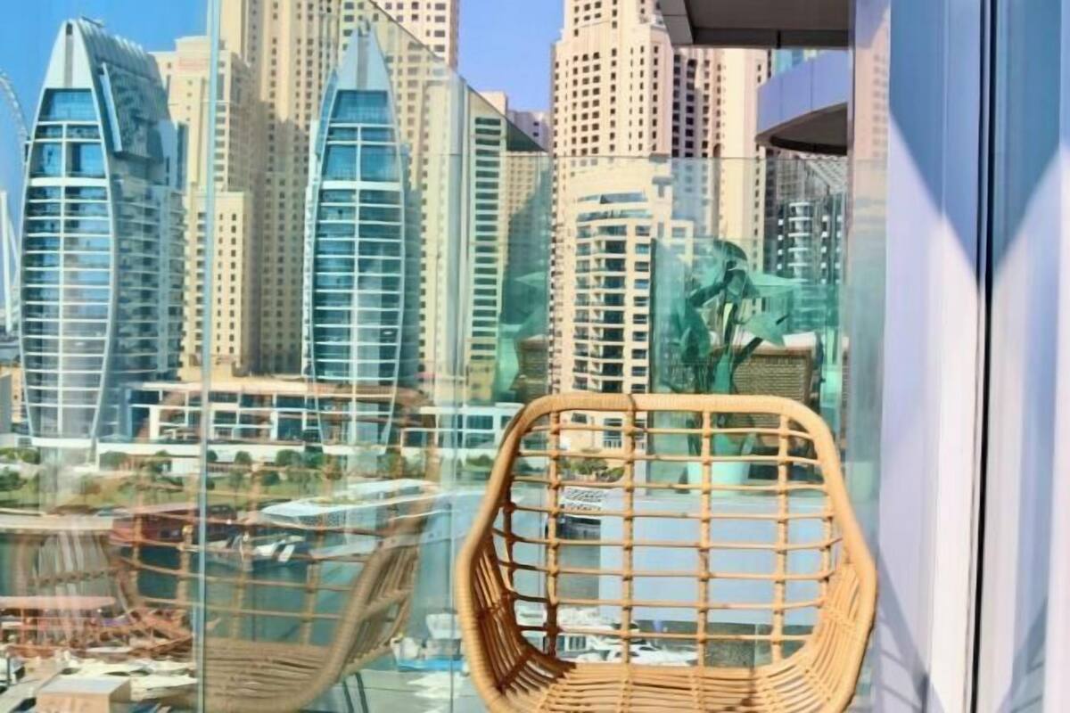 A high-rise building with a modern glass facade, a wicker chair, and a view of other tall buildings.