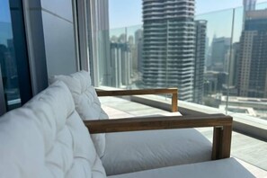 Una habitación moderna con un banco acolchado blanco junto a un ventanal grande, con vistas a edificios altos.