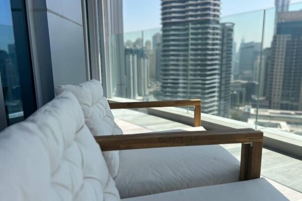 Una habitación moderna con un banco acolchado blanco junto a un ventanal grande, con vistas a edificios altos.