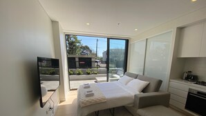 A modern bedroom with a large bed, a small sofa, and a kitchen area with a stove. - Executive Oasis | Chic 1BR + Courtyard Retreat (Engadine)